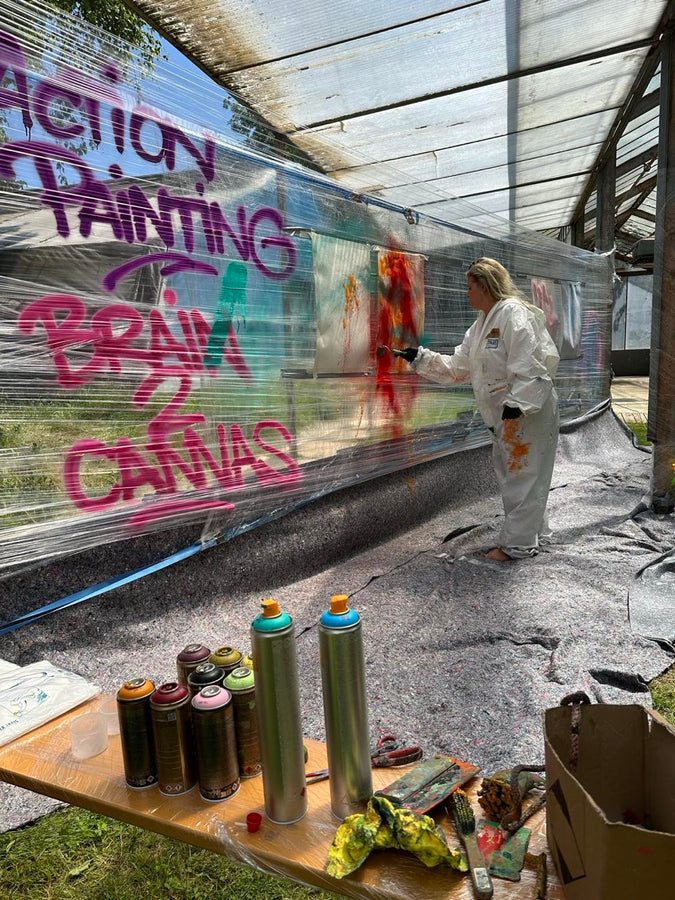 Teilnehmerin im Malanzug wirft Farbe auf eine grosse Leinwand beim Action Painting Team Event in München