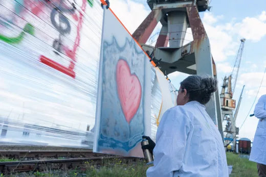HANSAINVEST-Teamevent am Hamburger Hafen: Teilnehmerin sprüht ein rotes Herz auf Leinwand, im Hintergrund alte Hafenkräne
