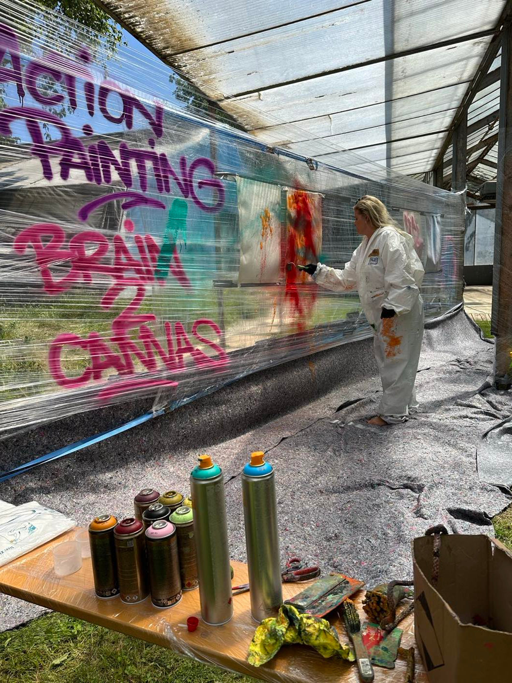 Teilnehmerin im Malanzug wirft Farbe auf eine grosse Leinwand beim Action Painting Team Event in München