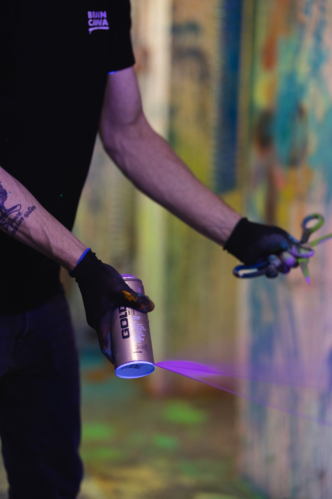 Hand sprueht mit UV-Farbe aus einer Spruehdose, violetter Farbstrahl im Schwarzlicht