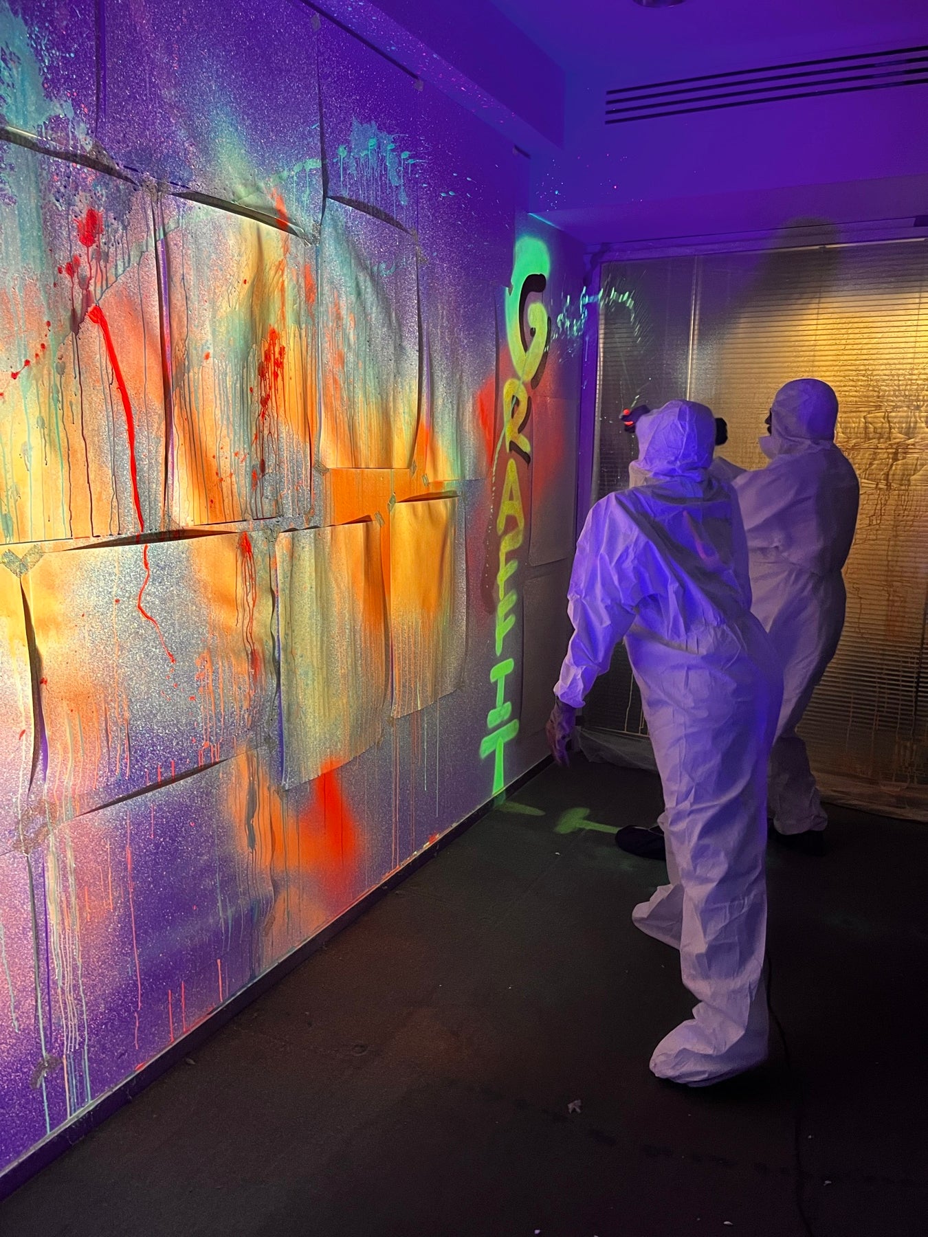 Action Painting unter Schwarzlicht: Team in weissen Maleranzuegen spruehte eine grosse Neon-Flaeche