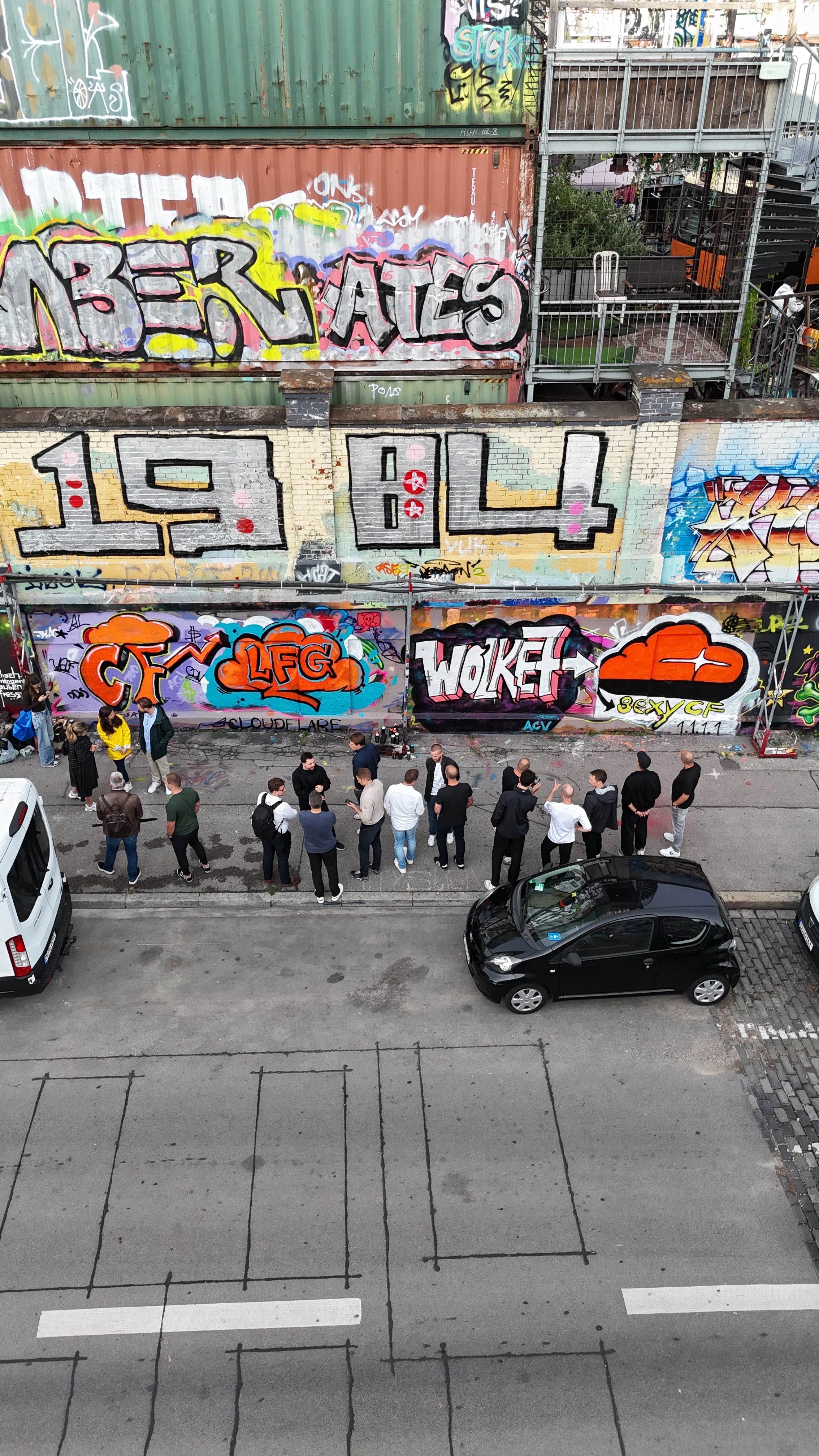 Luftaufnahme von oben: Team steht vor der frisch gesprühten Cloudflare-Wand mit Wolken-Logo und 1.1.1.1 am Bahnwärter Thiel
