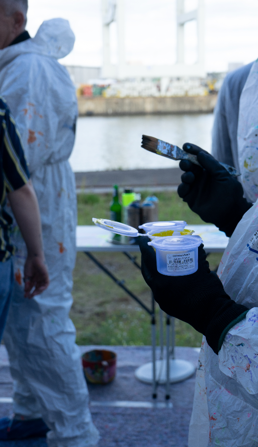 Zwei Teilnehmende in weißen Malanzügen mit Farbdosen und Pinsel am Pier vor der MS Bleichen