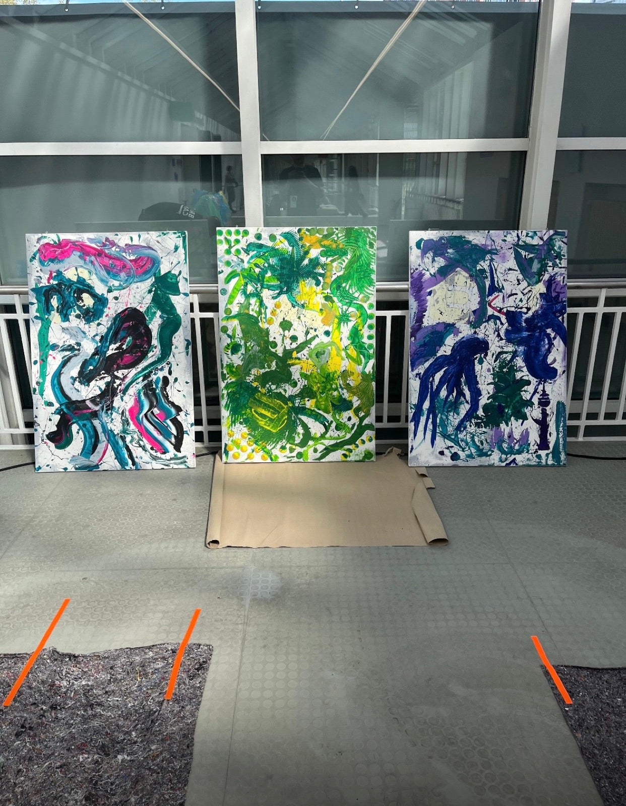 Drei fertige Action-Painting-Leinwaende eines Teams, aufgereiht im Tageslicht