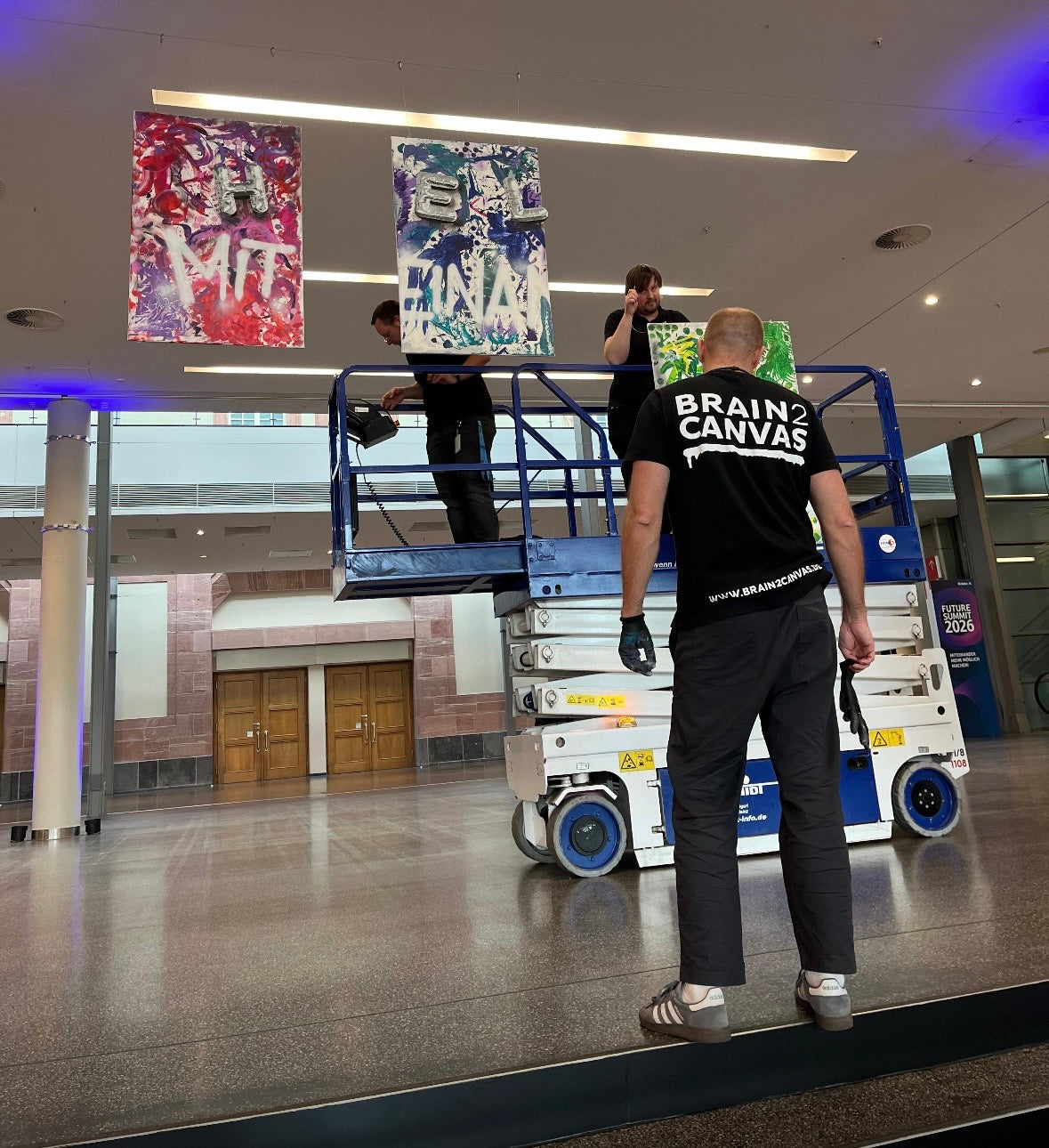 Drei fertige Hintergrund-Leinwände des Walk-in-Action-Paintings stehen am Geländer im Atrium