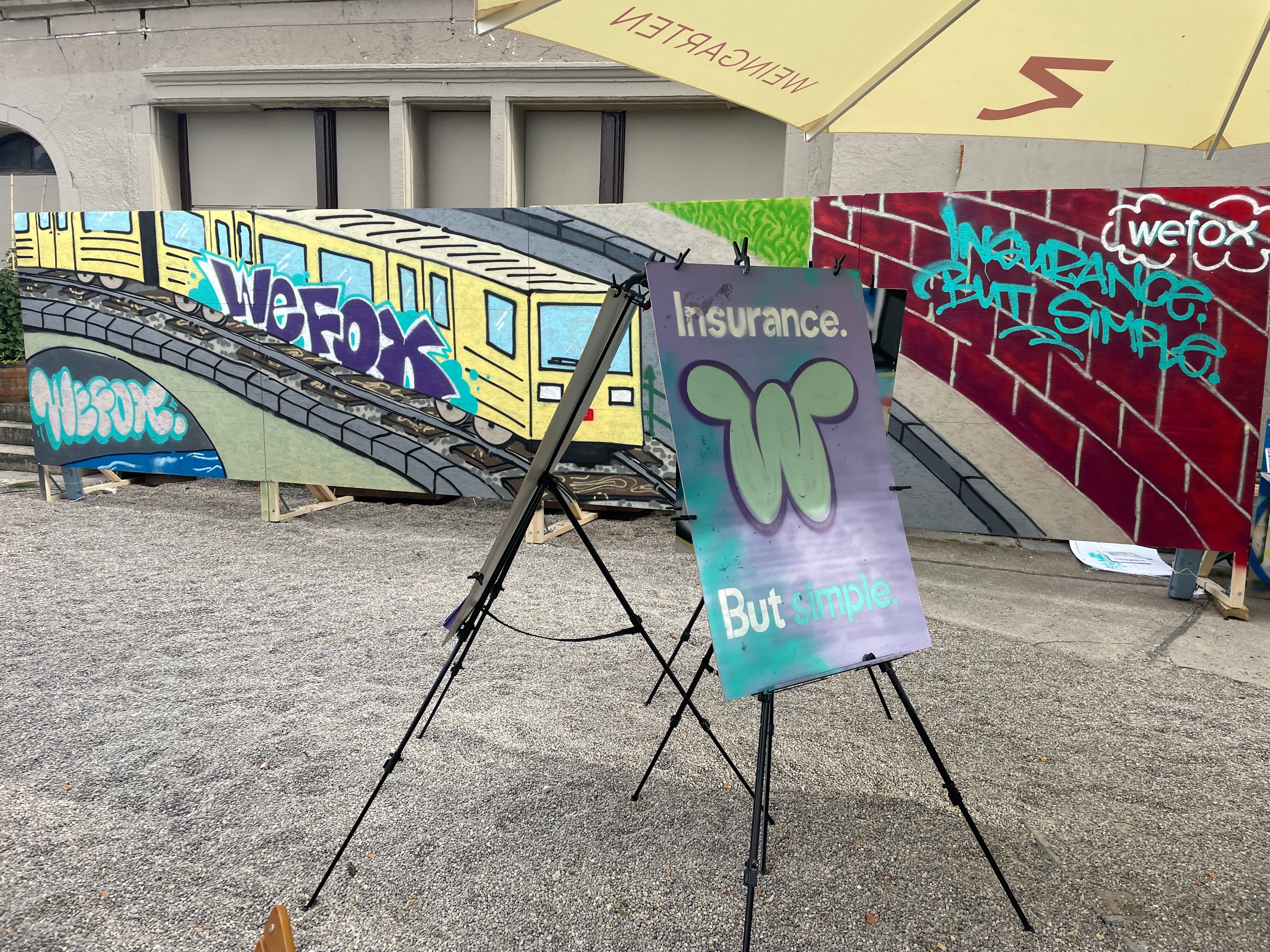 Sommerfest am Zenner: Gäste in besprühten Malkitteln arbeiten an Staffeleien, dahinter die mobile Graffiti-Wand mit U-Bahn-Motiv und wefox-Schriftzug