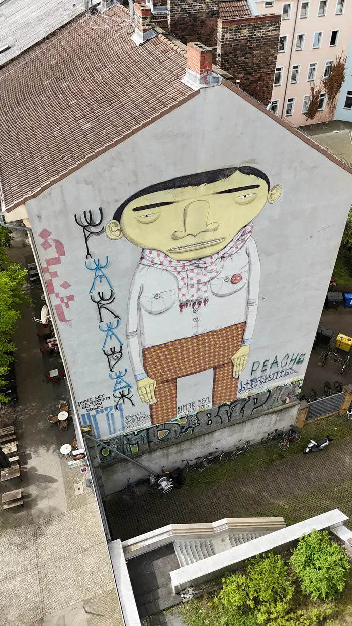 Eine gelbe Figur ueber eine ganze Brandmauer, von oben aufgenommen